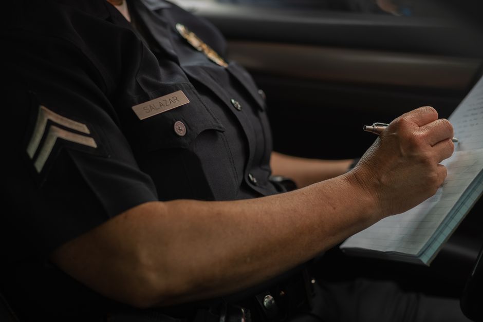 Close-up of a police officer writing in a notebook while sitting in a car, focused detail.